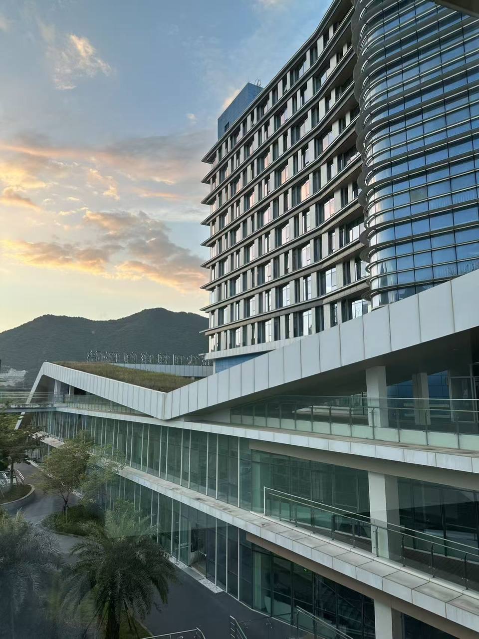 The hospital's ward tower at sunset, with the green roof of the therapy building and mountains behind
